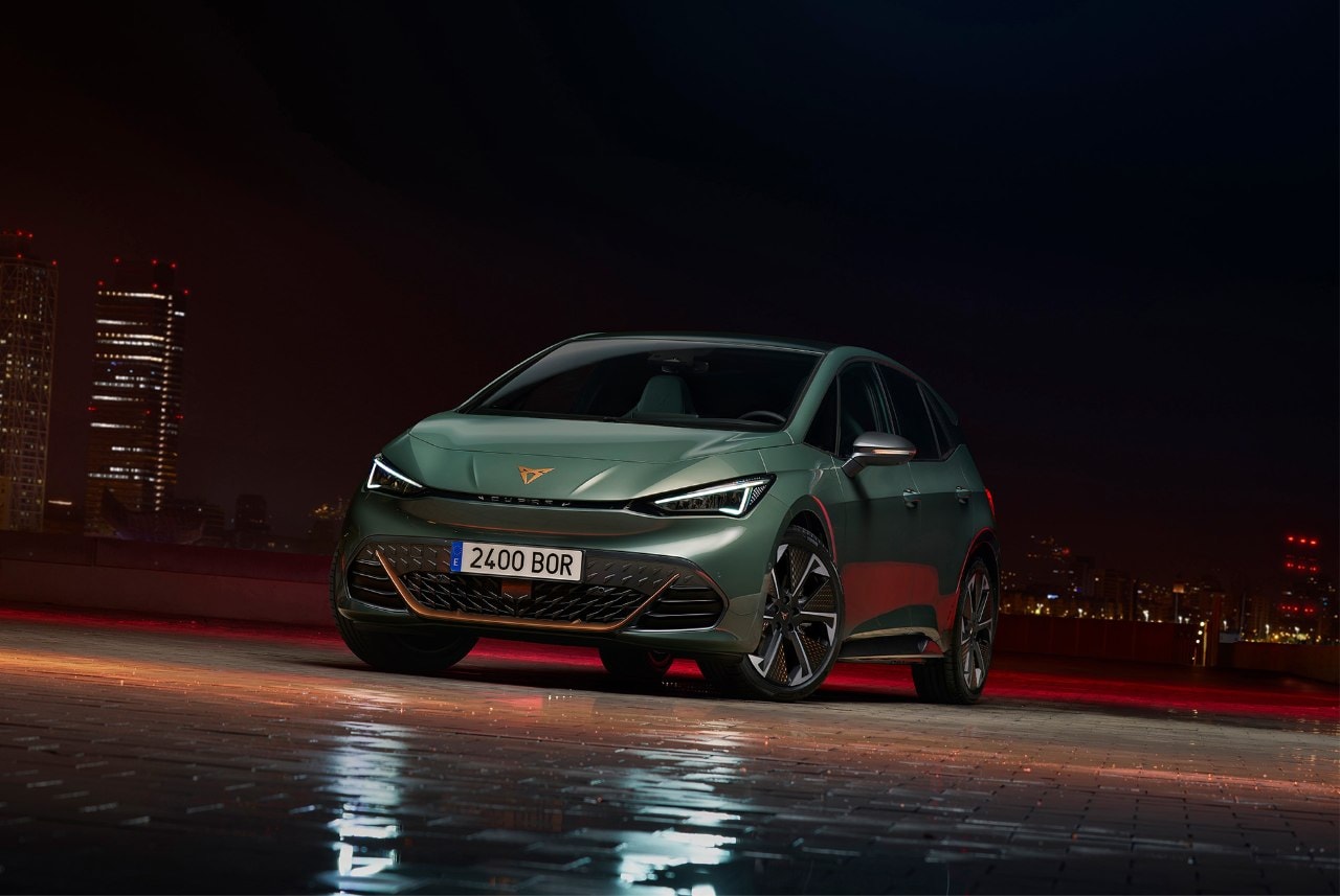 CUPRA Born en un entorno nocturno urbano con luces de neón reflejadas en el pavimento húmedo.