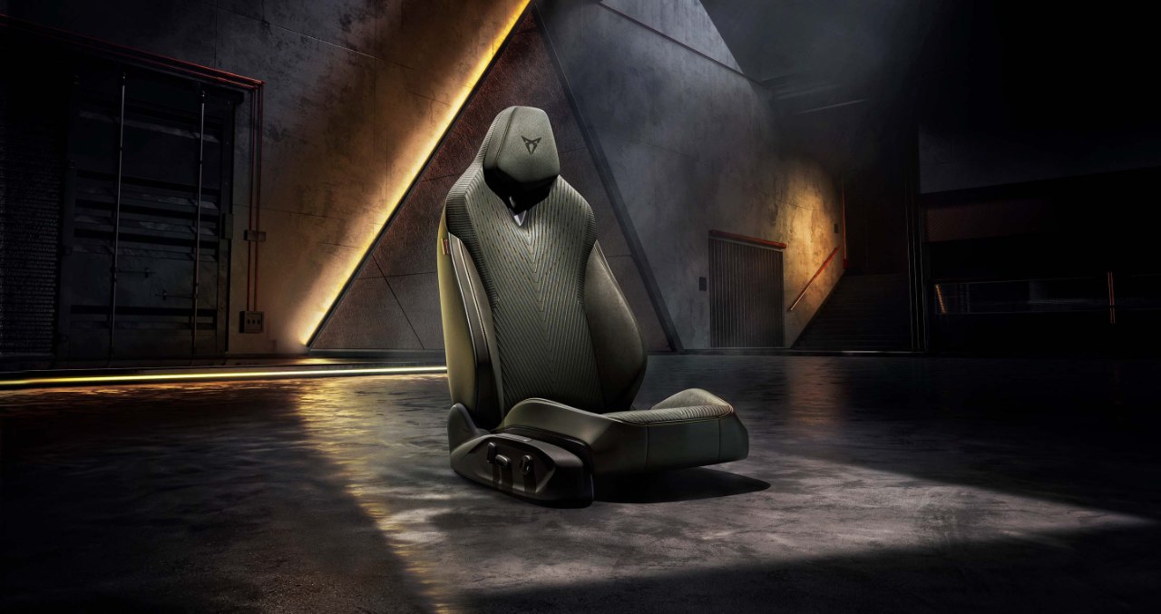 Single CUPRA Terramar sport car seat with ergonomic leather design and geometric details, illuminated under a spotlight in a dark, modern industrial setting.