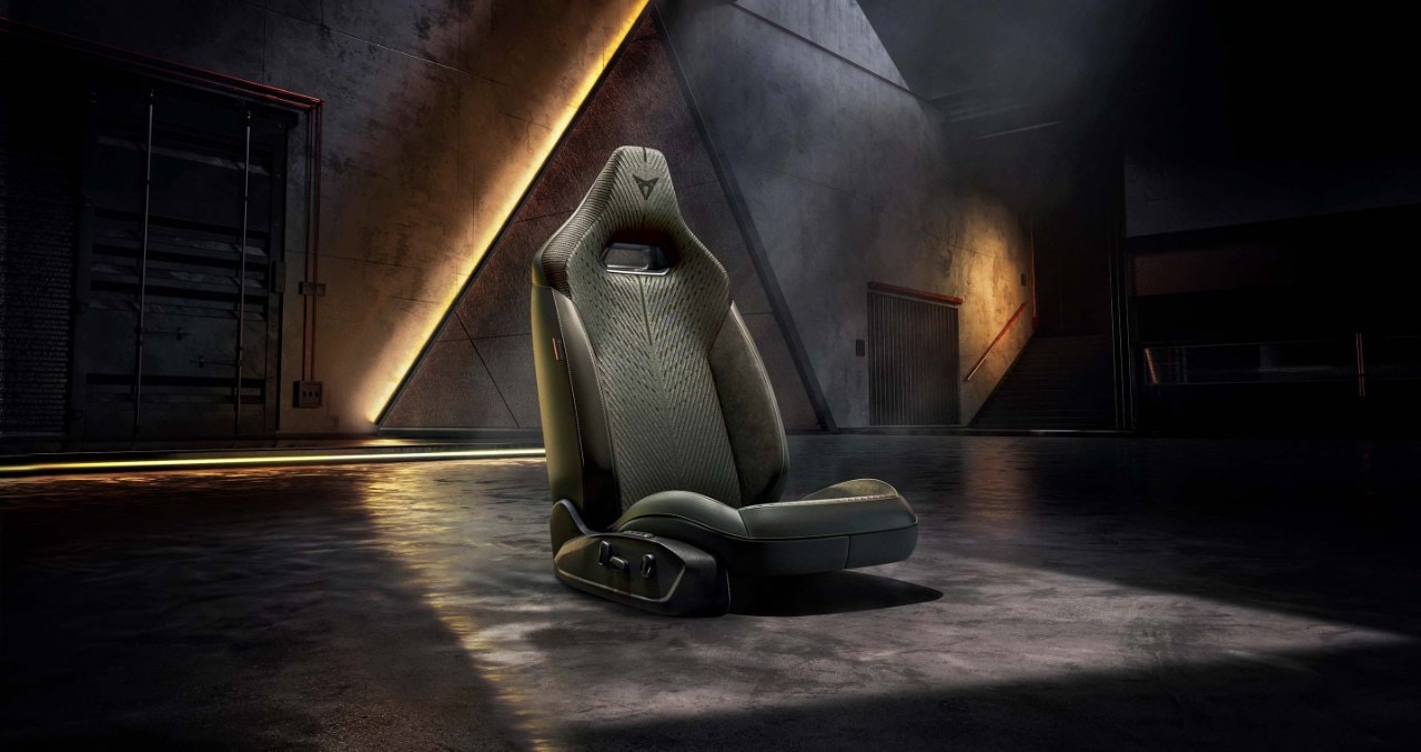 Single CUPRA Formentor sport car seat with ergonomic leather design and geometric details, illuminated under a spotlight in a dark, modern industrial setting.