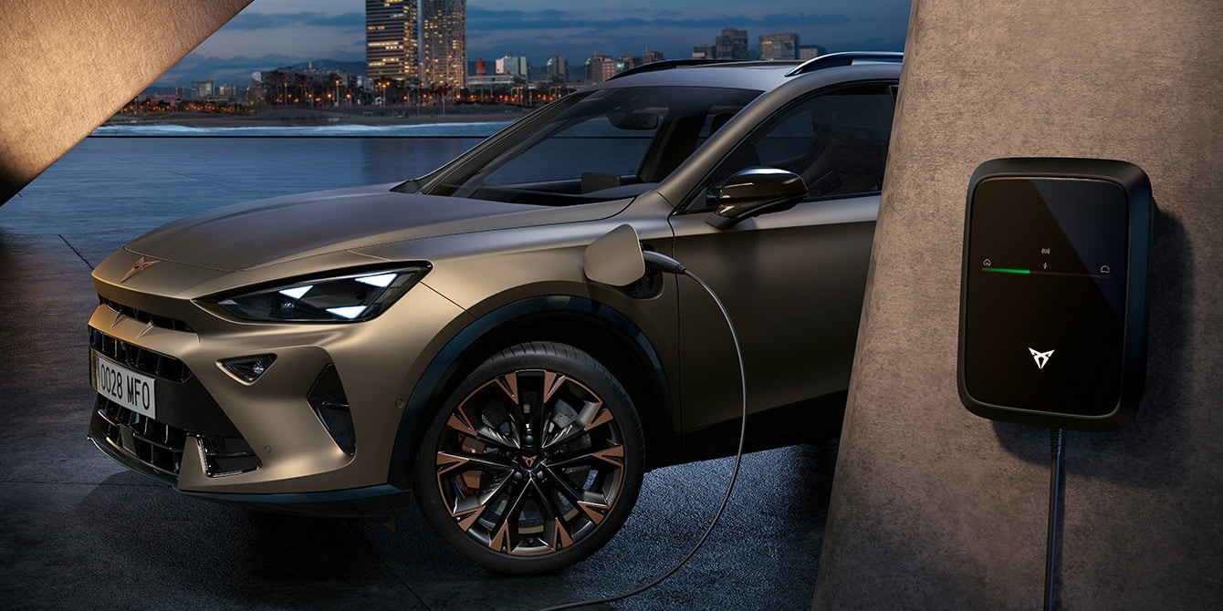 CUPRA Formentor e-HYBRID híbrido enchufable estacionado junto a un cargador en un espacio moderno.