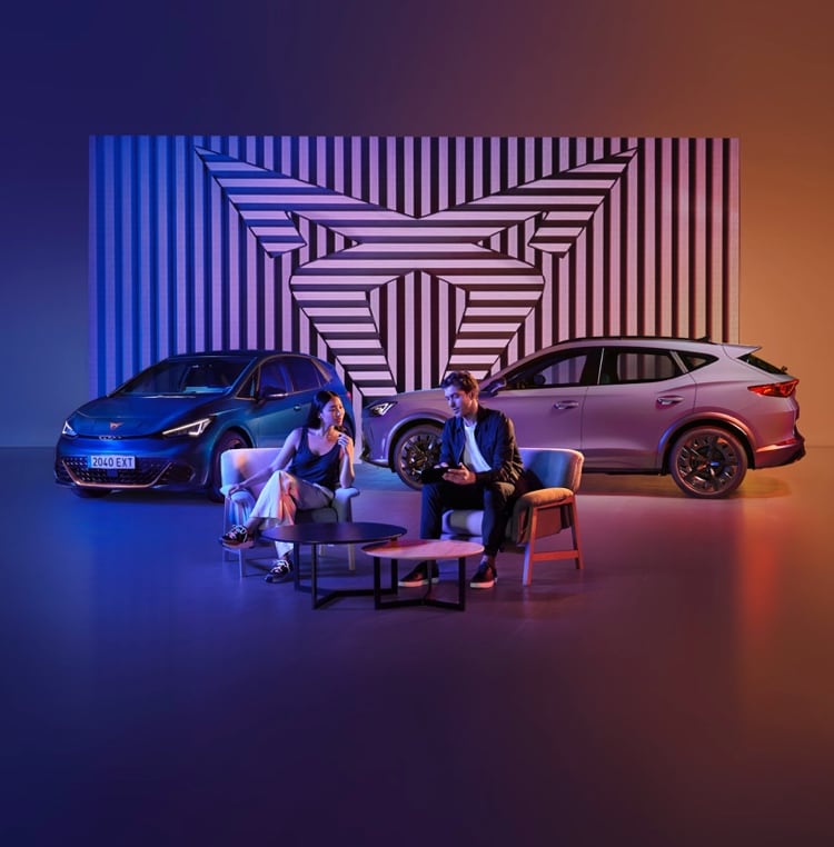 CUPRA Formentor y CUPRA Tavascan estacionados en un espacio futurista con luces de neón púrpura y naranja, junto a una pareja relajada en un lounge moderno.