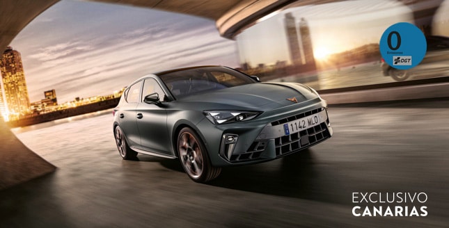 CUPRA León e-HYBRID en color gris circulando al atardecer frente a un skyline urbano, destacando su diseño deportivo y tecnología híbrida enchufable.