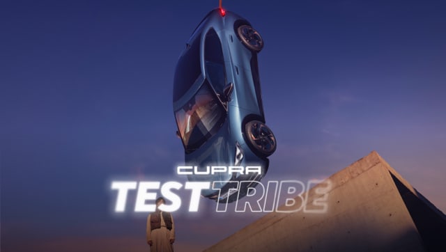 CUPRA Tavascan SUV coupé eléctrico sujetado en el aire junto a modelo asomado a cornisa de edicifio de hormigón.