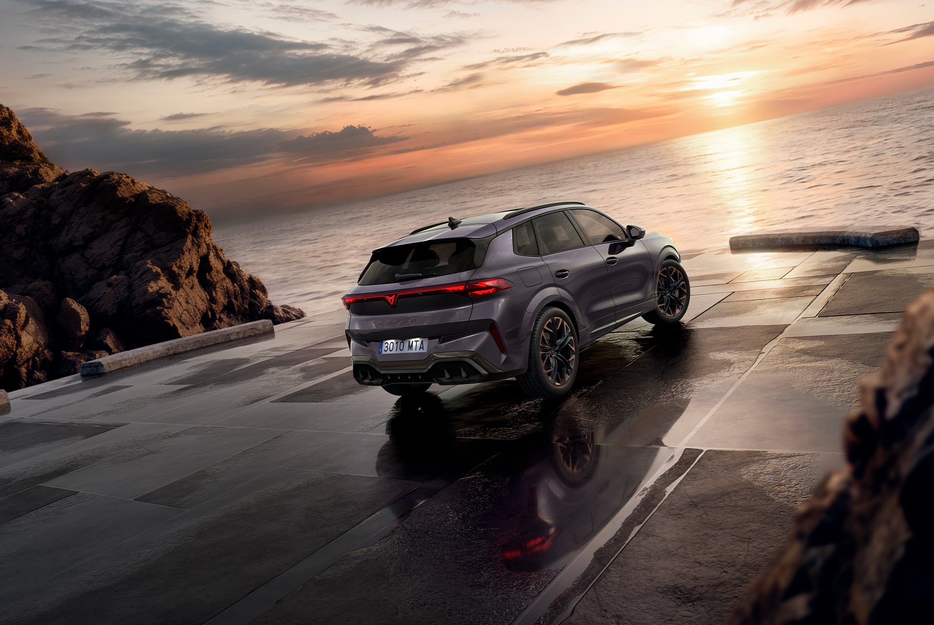 SUV híbrido CUPRA Terramar, nuevo modelo 2025, ángulo de visión trasera, con elegantes faros traseros con el logotipo de CUPRA, modernas llantas de aleación y una carrocería deportiva, sobre una acera mojada junto al mar. 