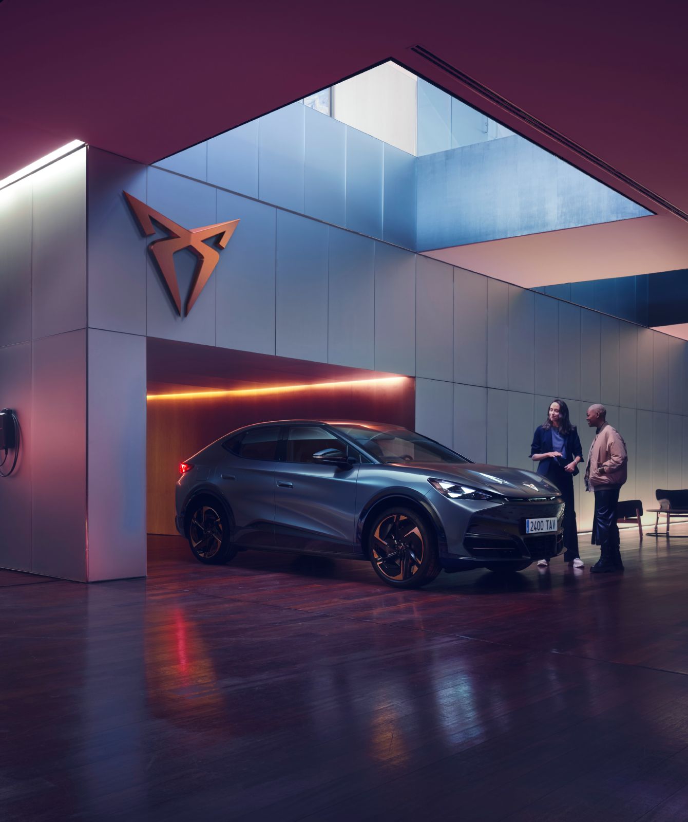 CUPRA Tavascan eléctrico en espacio de exposición moderno con iluminación ambiental púrpura.