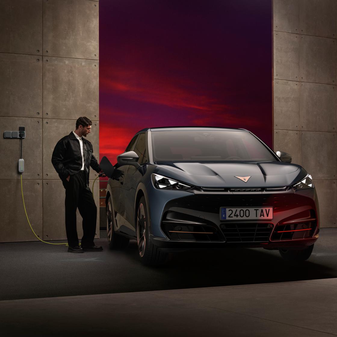 Hombre conecta cargador a CUPRA Tavascan eléctrico en escenario con cielo de color rojizo