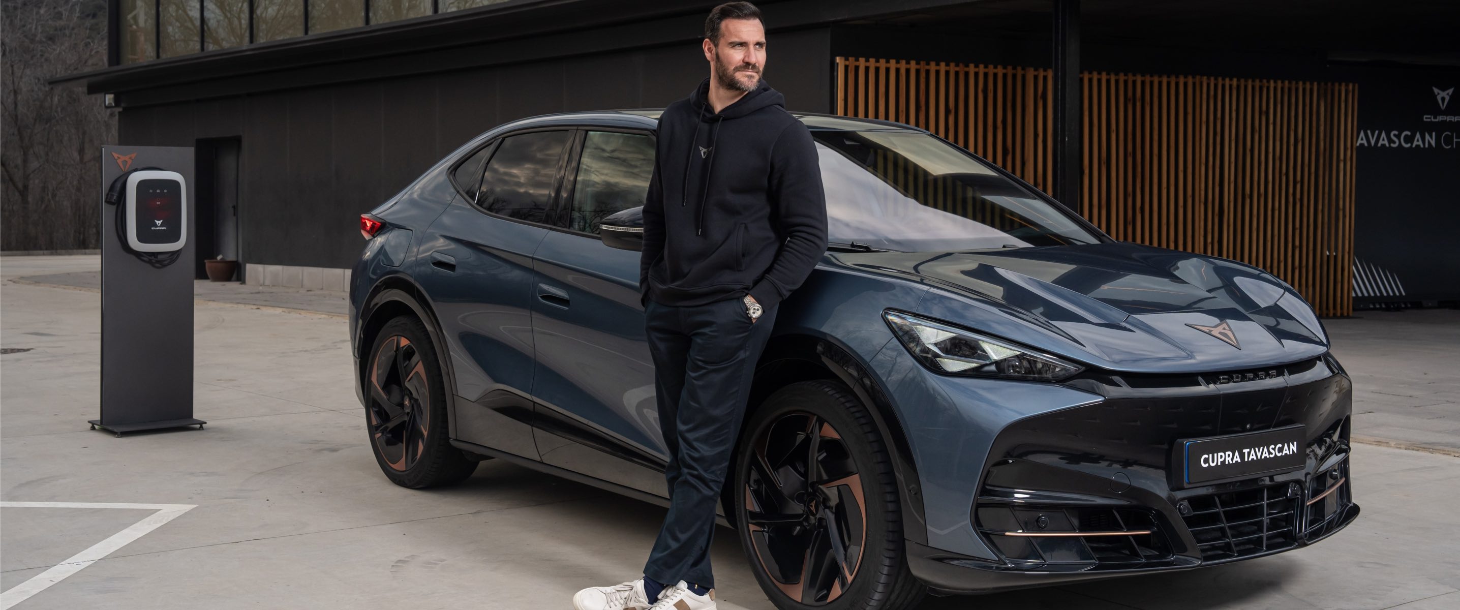 Saúl Craviotto apoyado en su nuevo CUPRA Tavascan junto a punto de carga pública