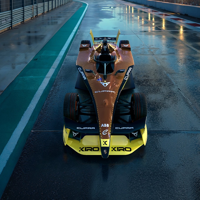 Vista frontal del CUPRA Kiro de Fórmula E, luciendo su librea inspirada en el diseño copper con audaces detalles en negro y amarillo, diseñado para la temporada 2025 de Fórmula E, sobre una pista de carreras mojada.