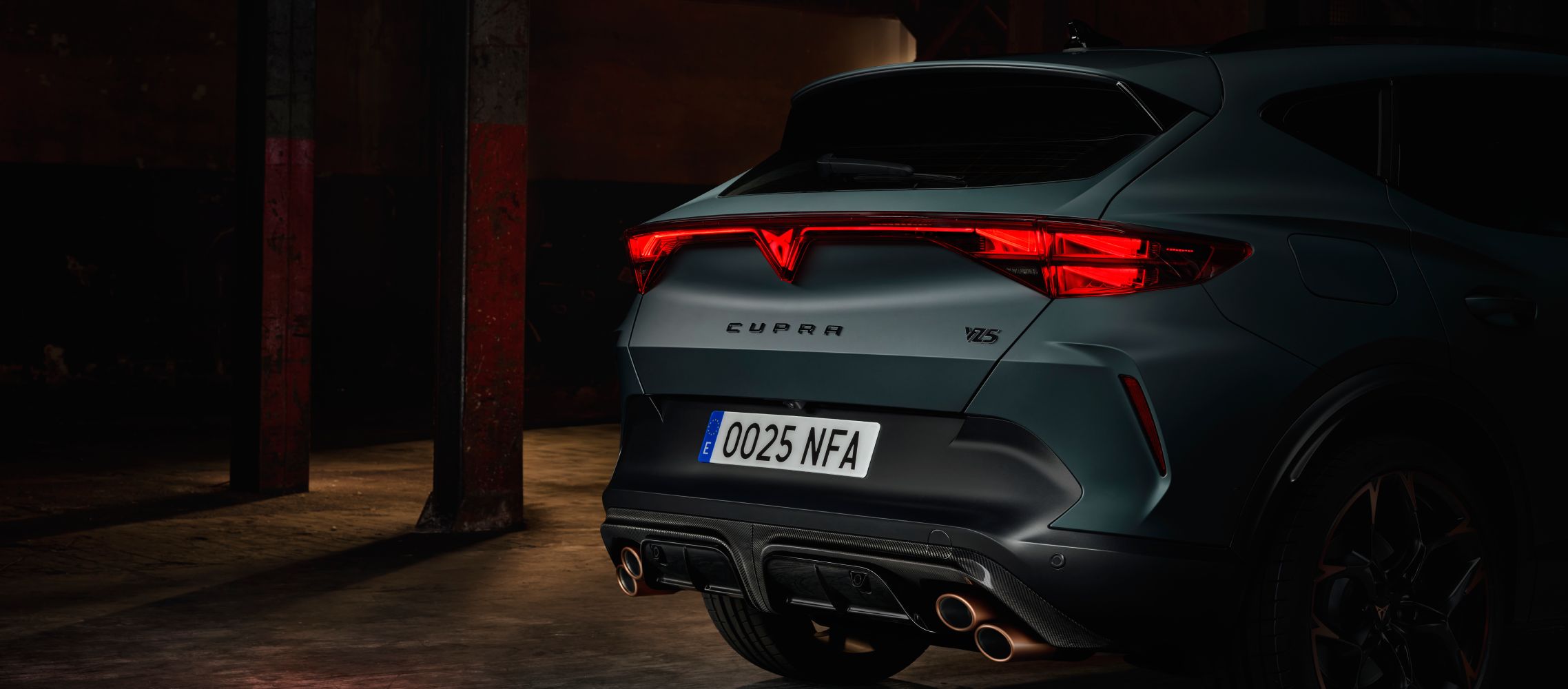 Primer plano trasero de un CUPRA Formentor VZ5 en entorno industrial con dos columnas metálicas en el fondo