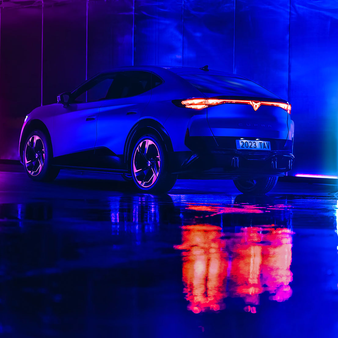 CUPRA Tavascan eléctrico sobre asfalto mojado con luces de neón púrpura y azul
