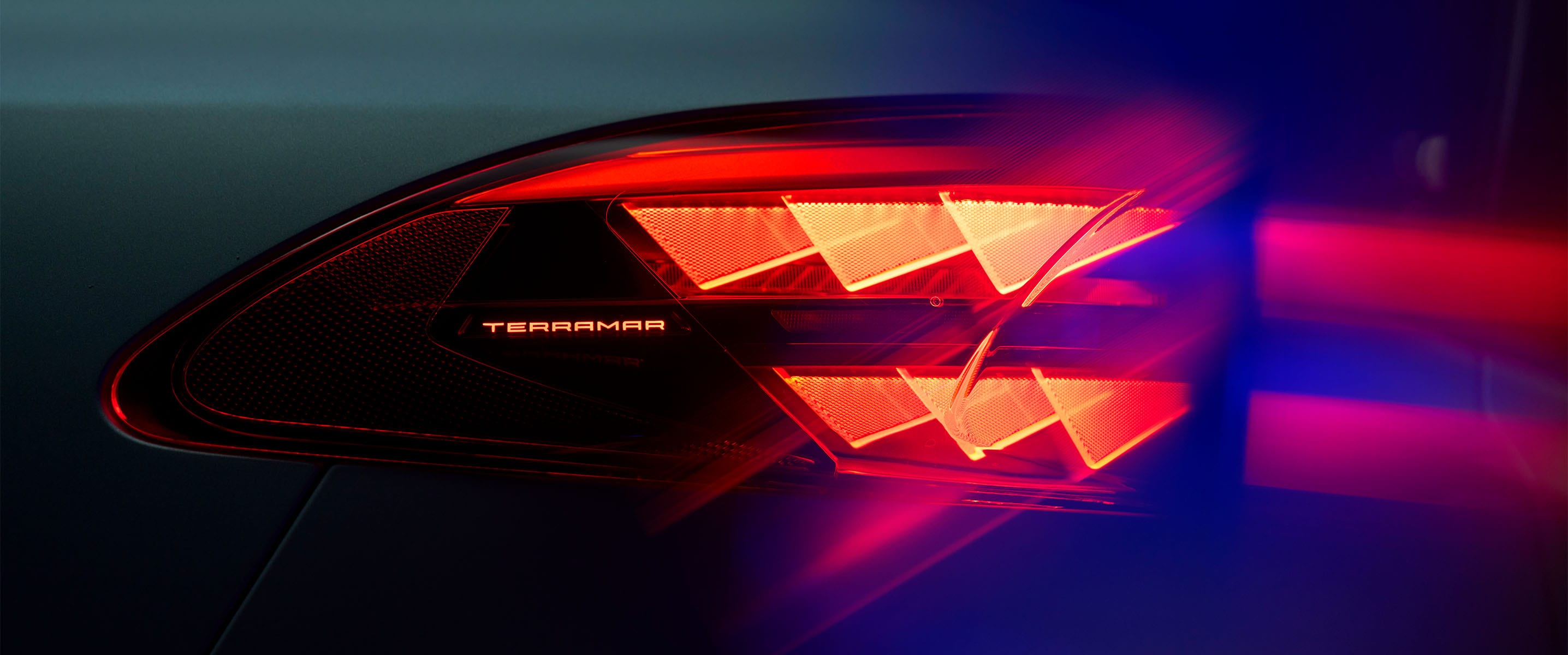 Primer plano de la luz trasera del CUPRA Terramar con el nombre del modelo iluminado, mostrando un distintivo patrón de luz triangular rojo contra un fondo oscuro.