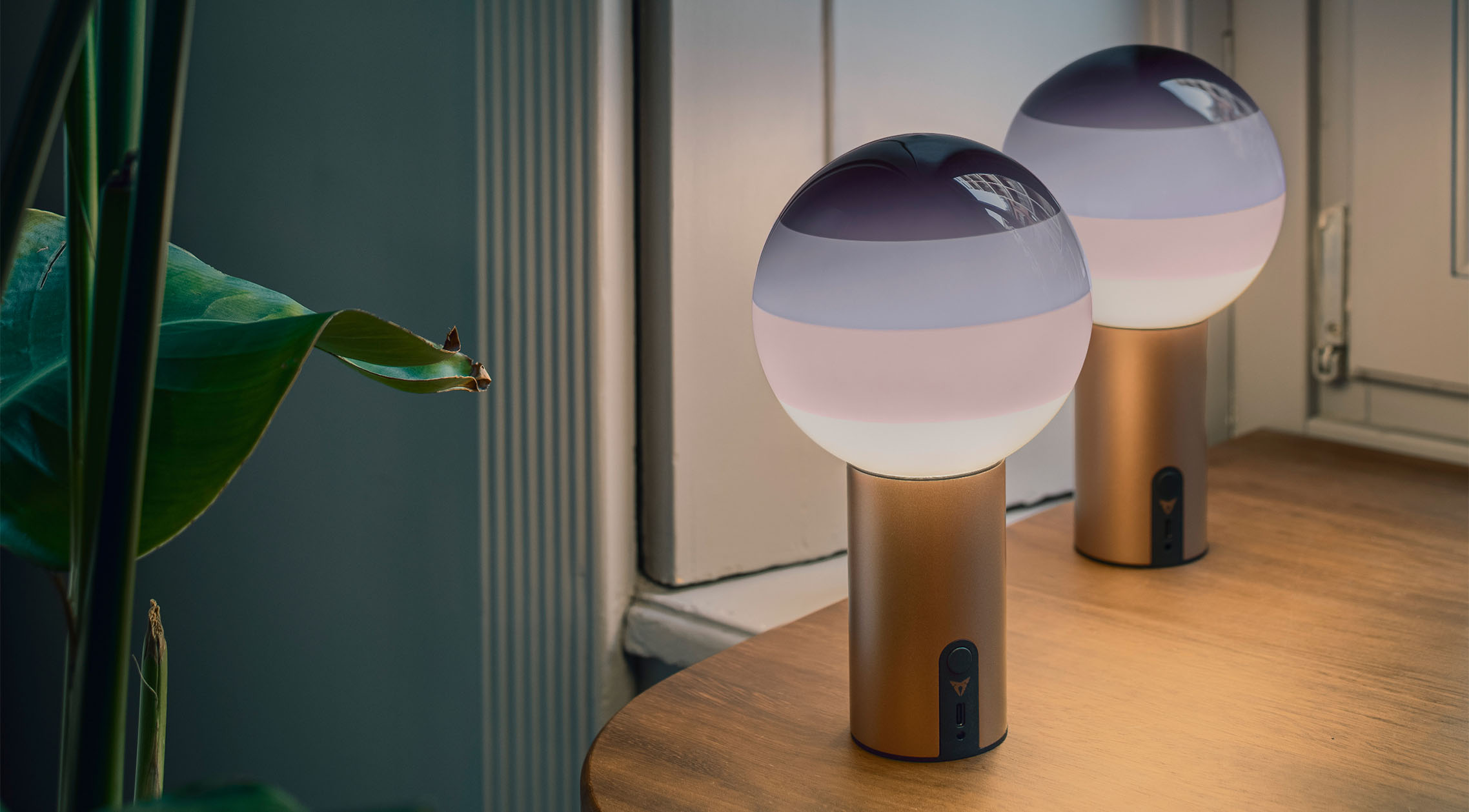two cupra x marset dipping lights with spherical frosted glass tops and purple gradients are lit, creating a warm, ambient light. The portable lamps’ metallic copper bases both have a switch. two cupra x marset dipping lights with spherical frosted glass tops and purple gradients are lit, creating a warm, ambient light. The portable lamps’ metallic copper bases both have a switch.