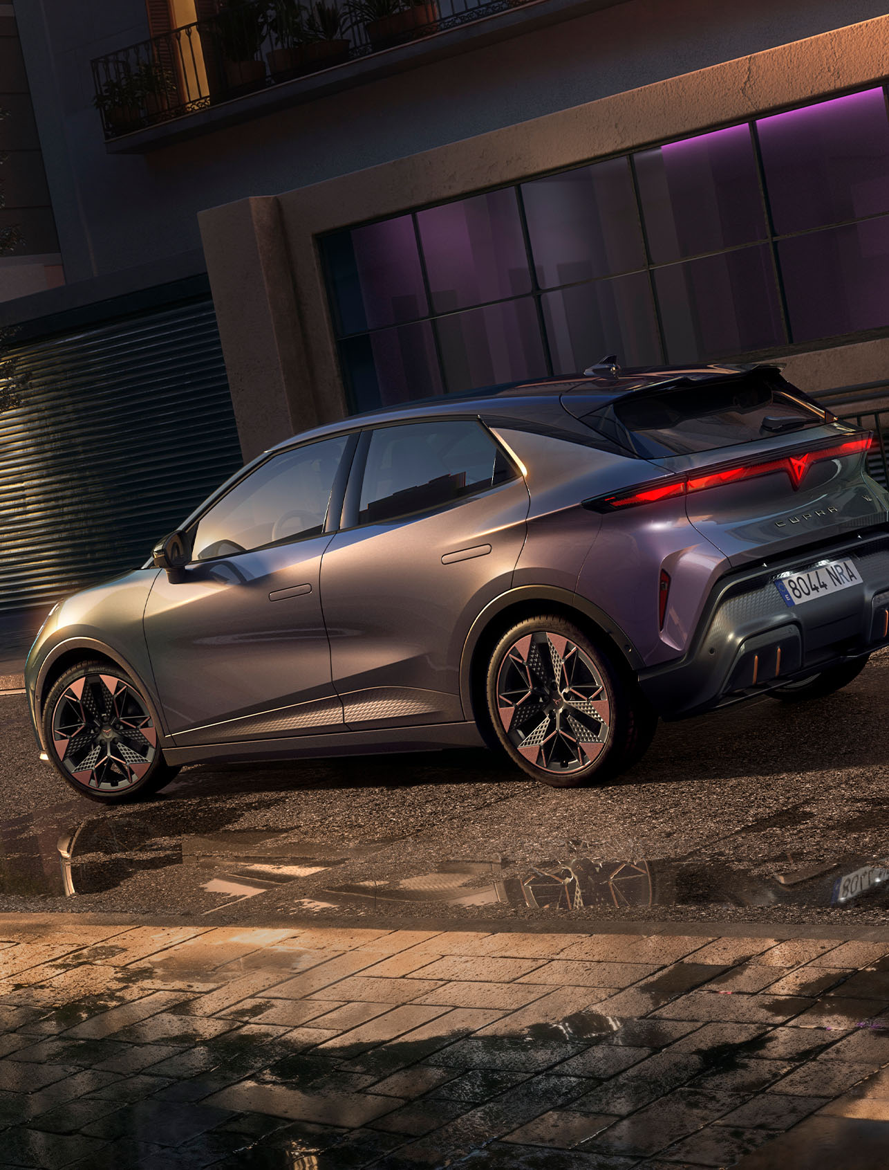 Primer plano de la parte trasera del CUPRA Raval VZ en color Plasma, con llantas de aleación de 48°cm (19”), aparcado en una calle de la ciudad por la noche.
