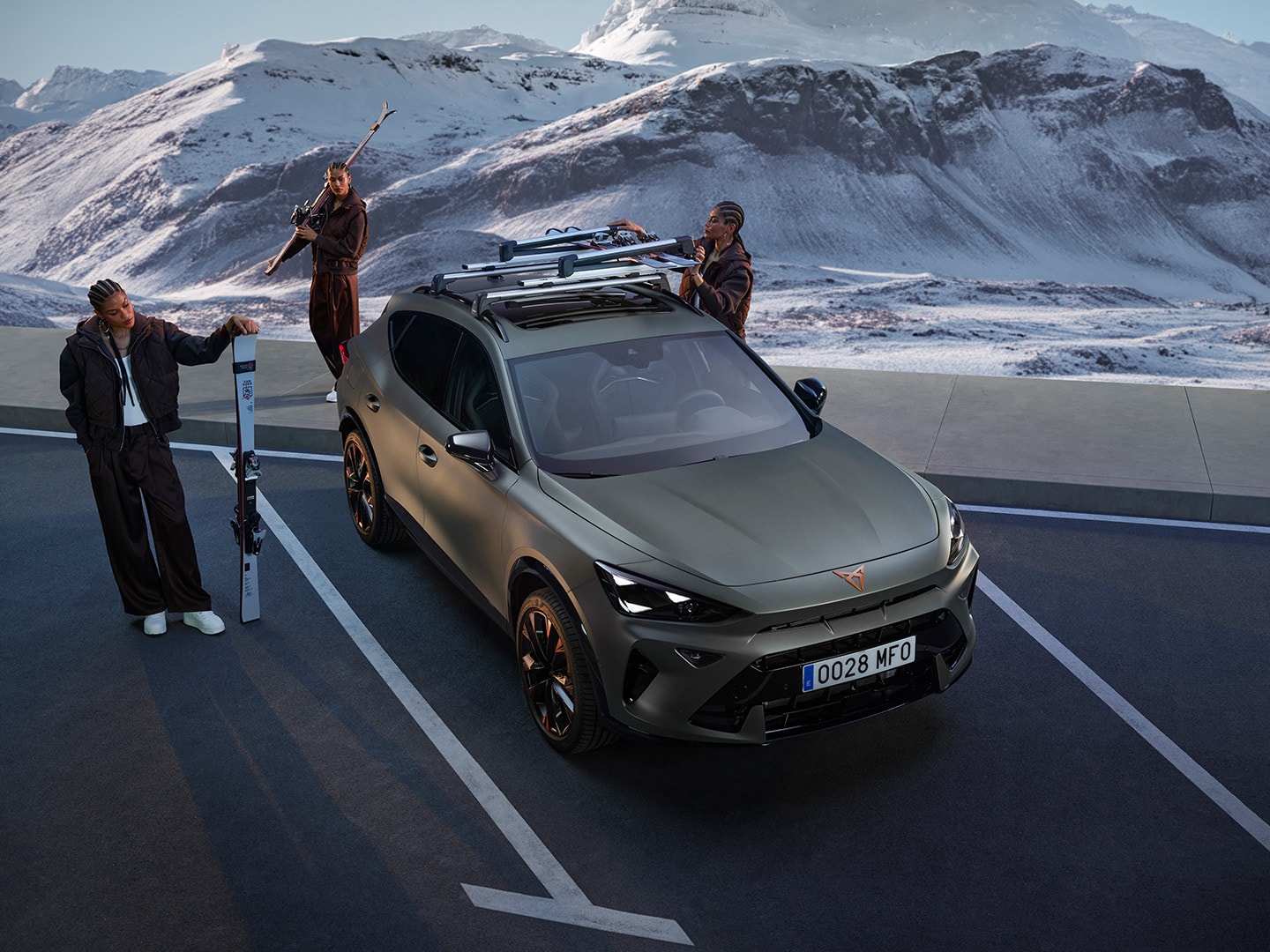 CUPRA Formentor con el portaesquís Xtender. Un CUPRA Formentor equipado con el portaesquís Xtender, con capacidad para 5 pares de esquís; al lado, unas personas preparándose para un viaje de esquí con una montaña nevada como paisaje de fondo.