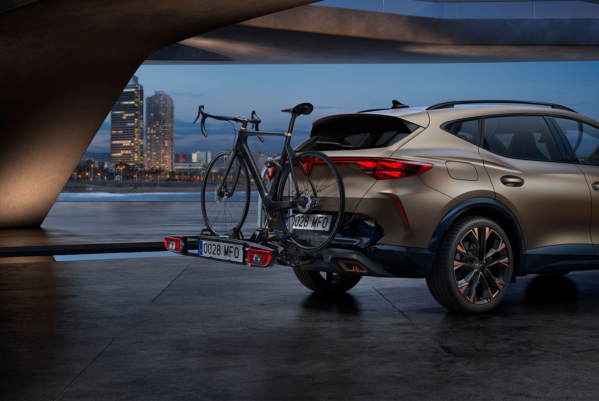 Nuevo CUPRA Formentor 2025 century bronze mate con remolque portabicicletas, horizonte de la ciudad de fondo.
