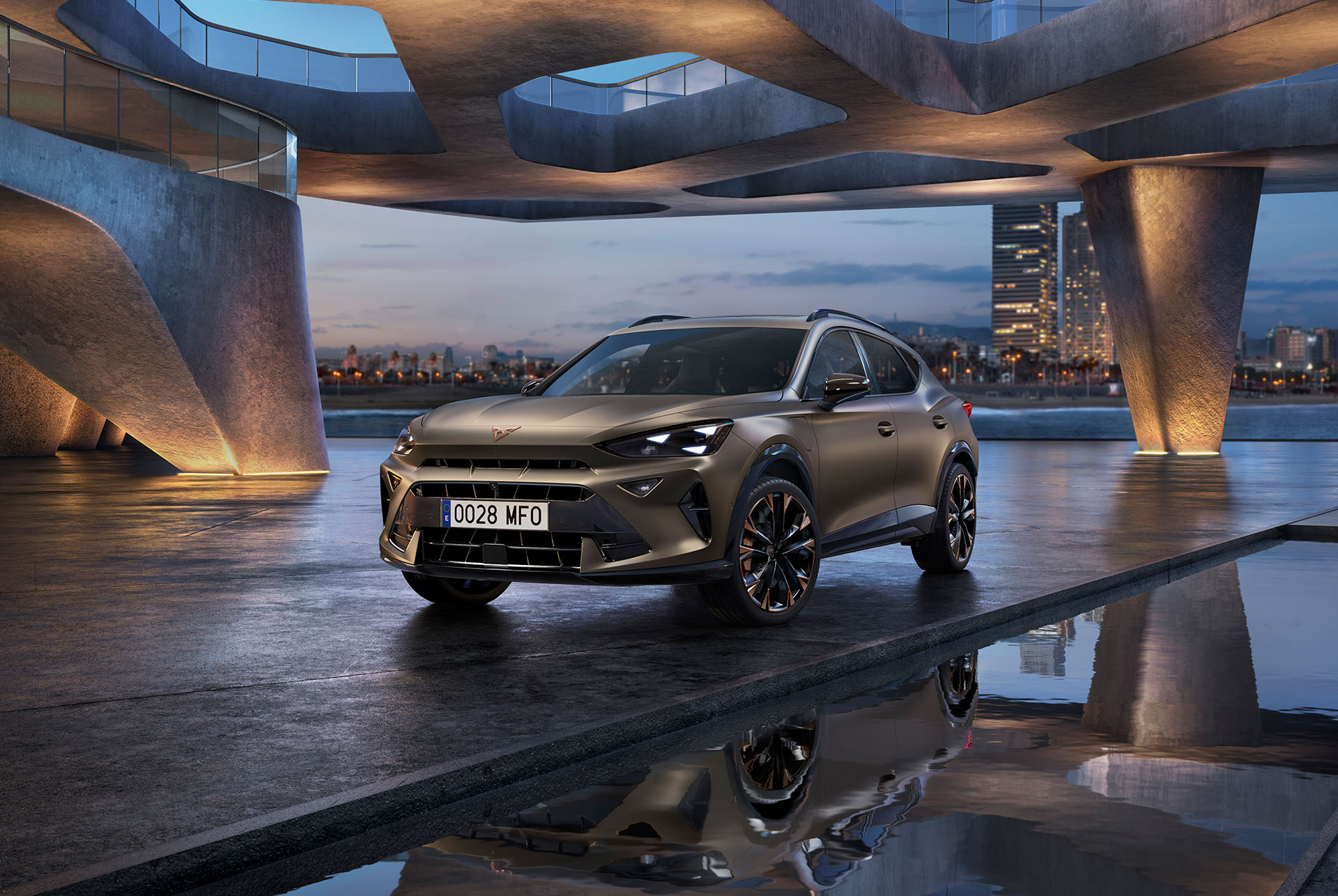 El CUPRA Formentor 2025 Century Bronze mate aparcado en un paseo marítimo que se refleja. El nuevo vehículo, deportivo y aerodinámico, se ubica en el centro del marco. En el escenario aparece una arquitectura futurista y el resplandeciente skyline de la ciudad de Barcelona al atardecer.