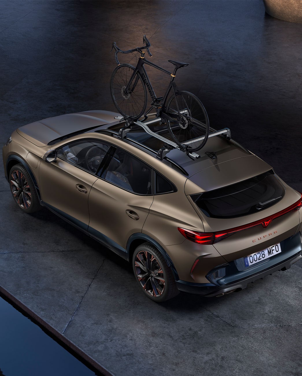 Vista de pájaro del nuevo CUPRA Formentor 2025 con el accesorio portabicicletas, aparcado en hormigón al atardecer.