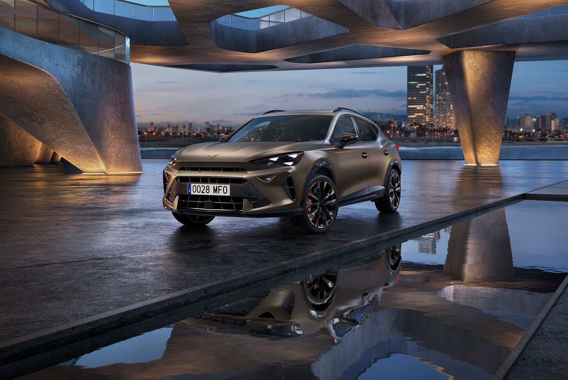 Tecnología del CUPRA Formentor CUV 2025. El coche con ruedas con acabado en Copper está aparcado bajo una estructura curva de hormigón cerca de una superficie de agua reflectante, con un paisaje urbano al atardecer de fondo con rascacielos iluminados.