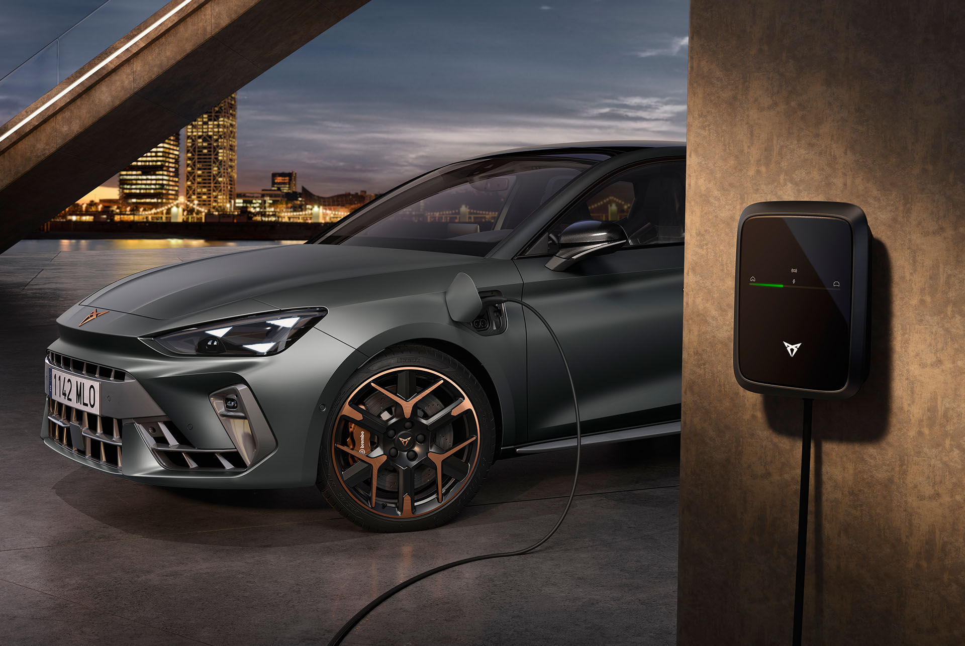 Vista frontal lateral del nuevo vehículo híbrido CUPRA León Sportstourer 2025 en Enceladus Grey, enchufado y cargando. Diseño angular de los faros y llantas de aleación con detalles en cobre.