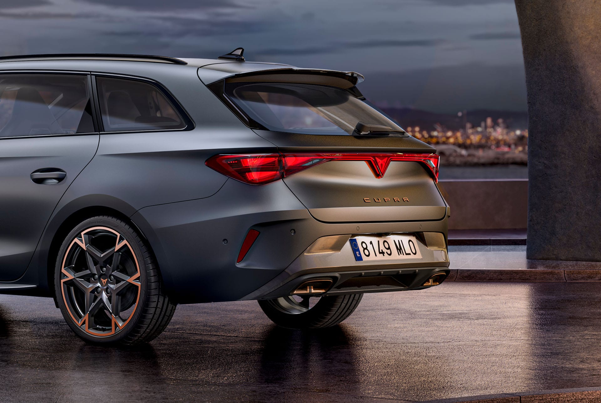 primer plano de la vista lateral trasera del nuevo coche híbrido CUPRA León 2025 Enceladus Grey 2024, llantas forjadas con acabado en cobre, estructura de hormigón y skyline de la ciudad