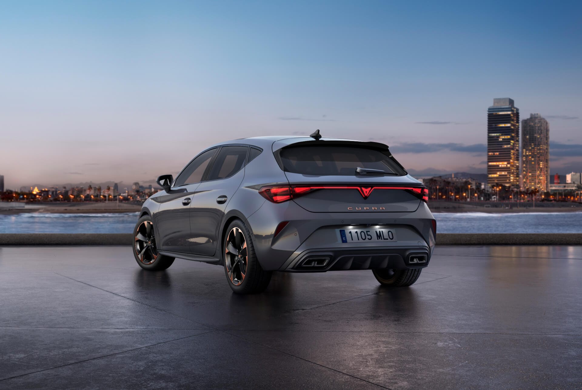 Vista trasera del nuevo modelo de coche CUPRA León 2025 gris brillante con control de chasis adaptativo y llantas de aleación en negro y cobre. Ciudad al fondo al atardecer.