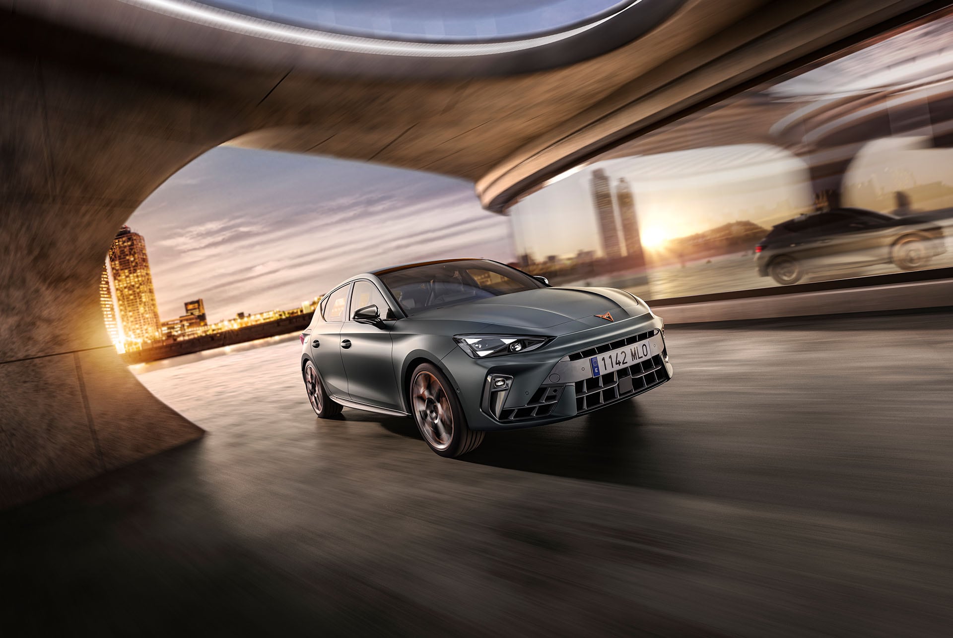 Volante del nuevo CUPRA León 2025, selección del perfil de conducción de Infotainment, tecnología avanzada de dirección, opción de control de chasis adaptativo, salpicadero, ventanilla y skyline de la ciudad