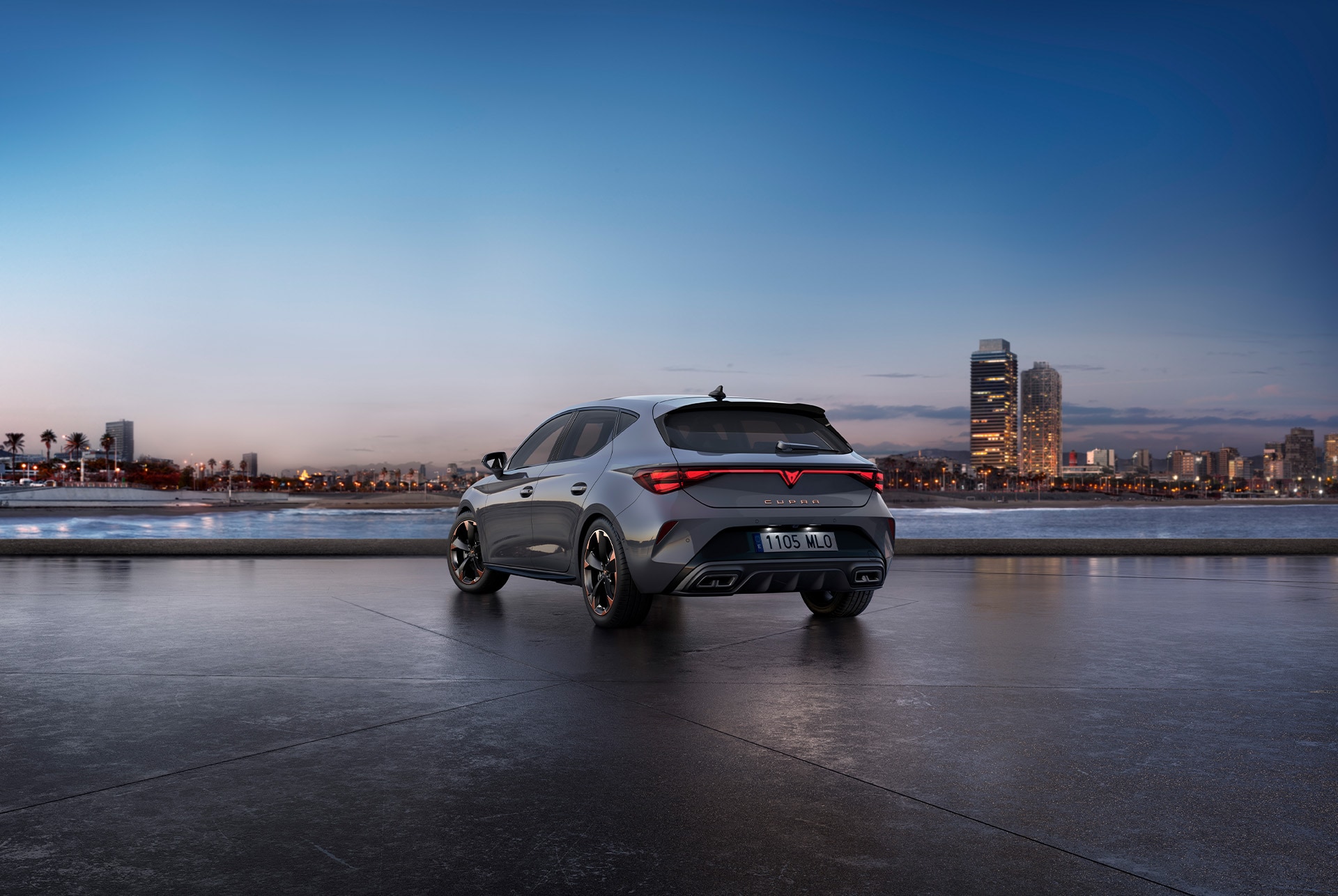 Vista trasera del modelo de coche CUPRA León gris brillante con control de chasis adaptativo y llantas de aleación en negro y cobre. Ciudad al fondo al atardecer.