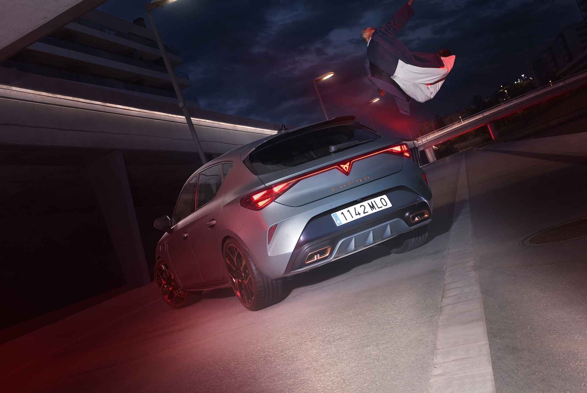 Tecnología del CUPRA León e-Hybrid, iluminación trasera LED, vehículo Híbrido Enchufable aparcado sobre cemento, estructura con bordes brillantes. El vehículo se muestra en acabado gris mate con llantas forjadas en cobre y negro.