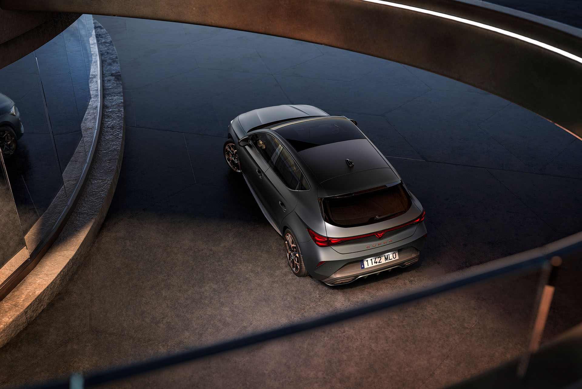 Vista de pájaro en tres cuartos de la parte trasera del nuevo CUPRA León 2025, escenario oscuro y reflejo en el retrovisor de la parte delantera.