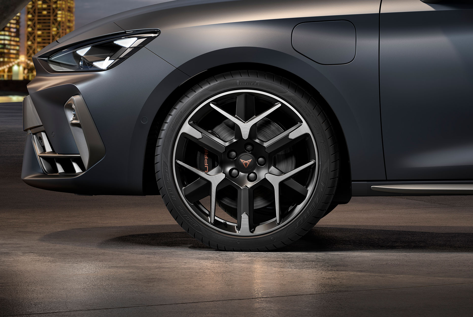 vista lateral delantera de la llanta forjada izquierda en plateado y negro para el nuevo CUPRA León 2025, neumáticos, faros característicos y carrocería gris mate del coche