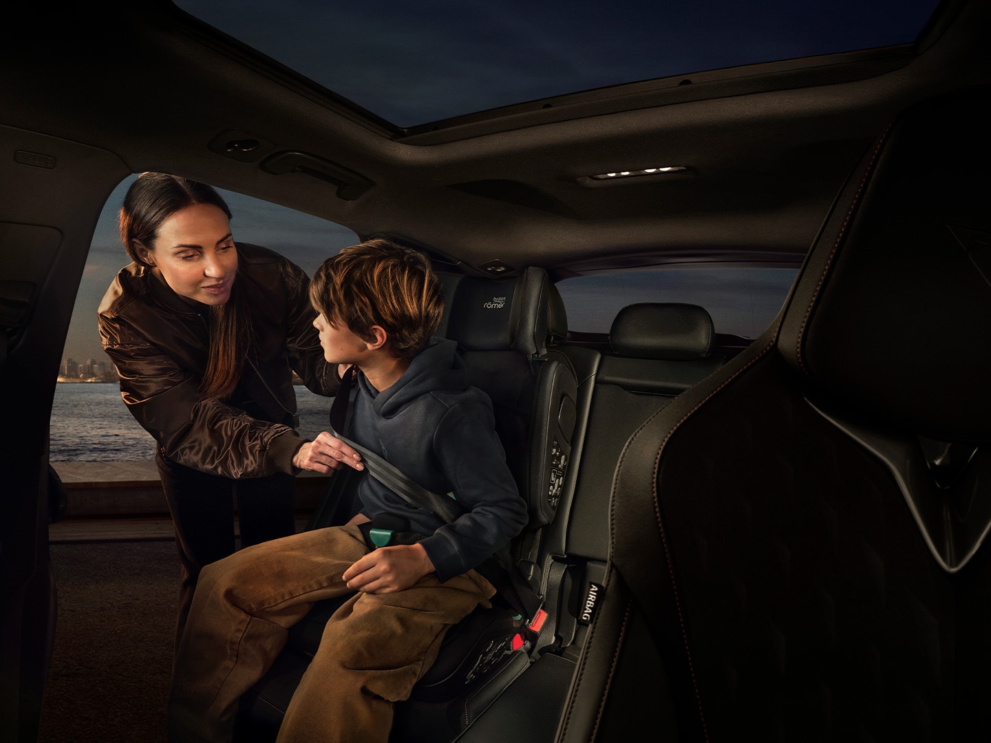 Vista del interior del CUPRA Terramar en la que se muestra el asiento trasero. Hay una mujer sujetando un niño en el asiento de seguridad para niños.