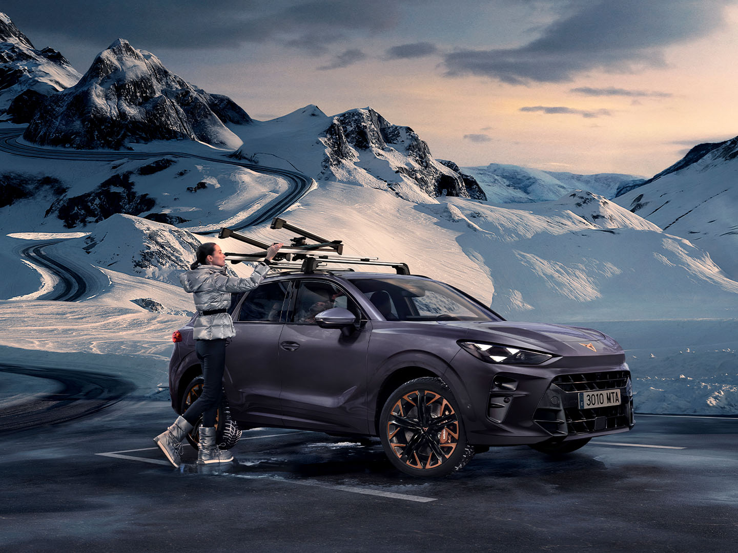 CUPRA Terramar en un paisaje nevado, mostrando el portaesquís, uno de sus accesorios de transporte, montado en el techo. Hay una mujer utilizando este portaesquís para transportar sus esquís.