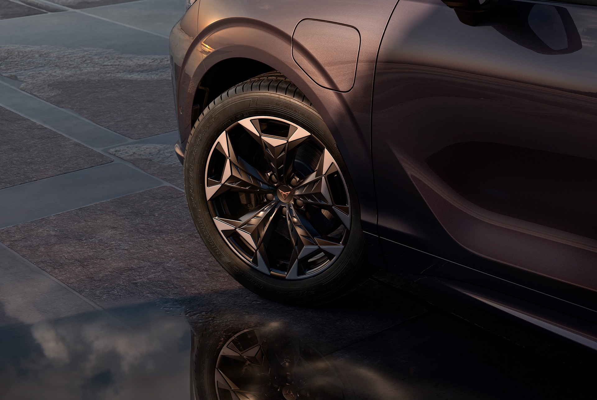 Llantas de aleación Cosmic de 48 cm (19") en negro con detalles en cobre en el nuevo CUPRA Terramar. En el fondo hay una acera de baldosas y parte de la carrocería brillante y oscura del coche.
