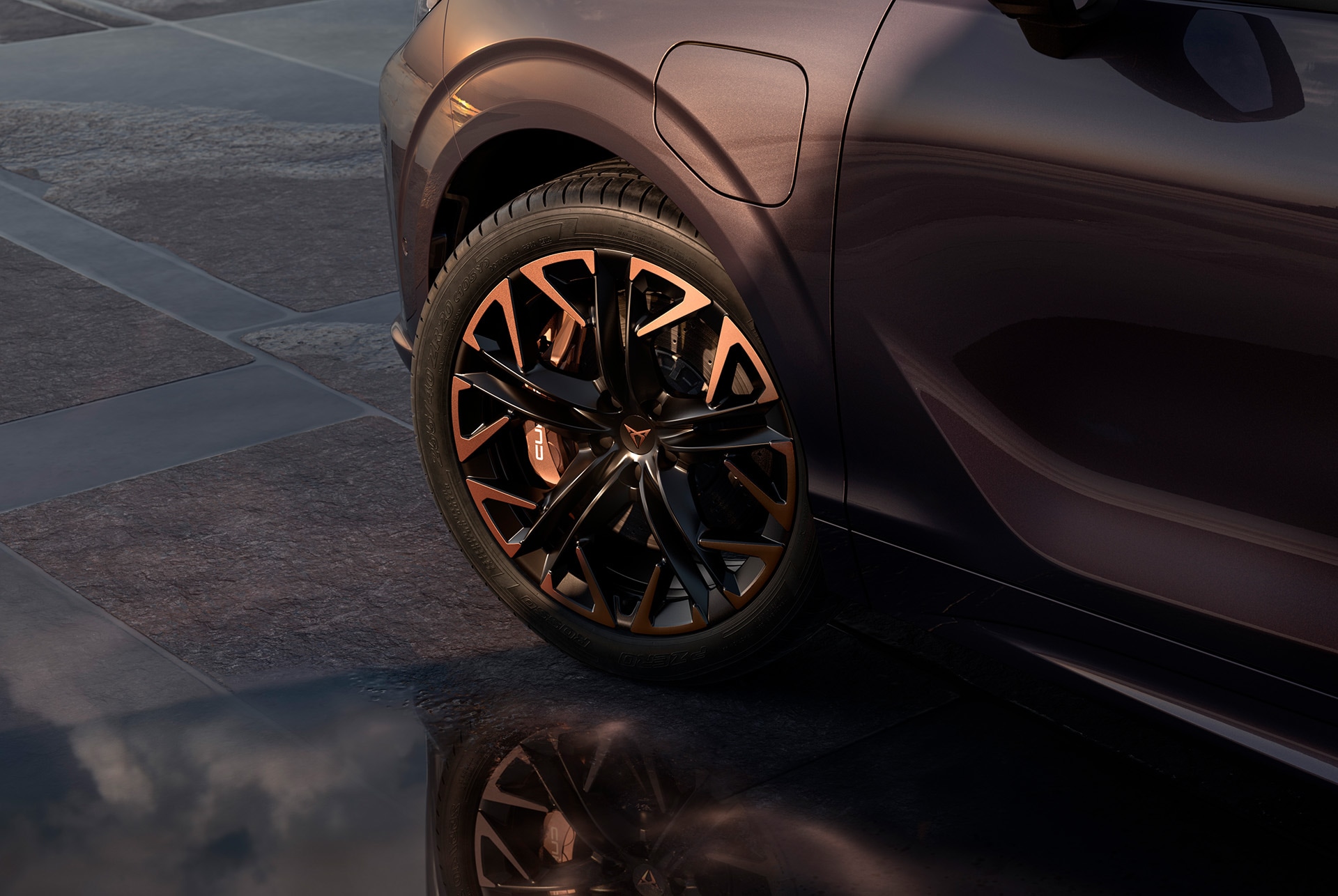 Llantas de aleación Handron Copper de 50,8 cm (20") en negro con detalles en cobre del nuevo CUPRA Terramar. Al fondo, acera de baldosas y parte de la carrocería brillante y oscura del coche.