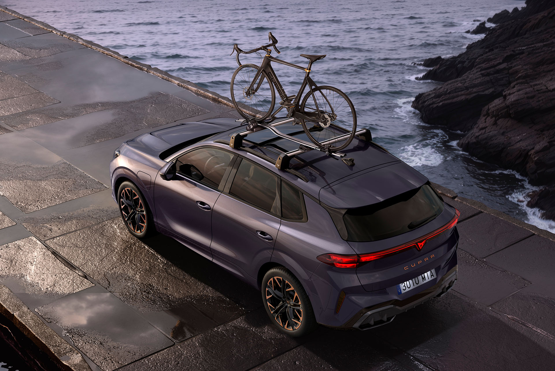 CUPRA Terramar con portabicicletas para dos bicicletas. El SUV está aparcado en una carretera costera, mostrando la facilidad de colocación del portabicicletas y su sistema antirrobo seguro, listo para la aventura.
