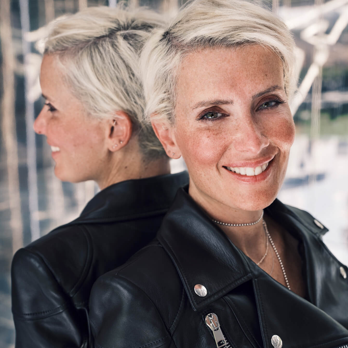 Cécilia Taïeb, con la espalda apoyada en un espejo, sonriendo con una cazadora de cuero negro.