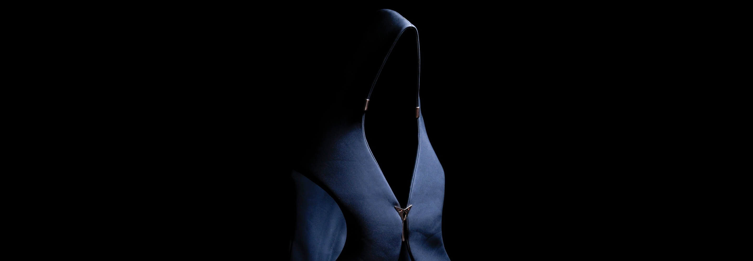 Una prenda oscura con capucha y una cremallera prominente aparece iluminada de forma espectacular sobre un fondo negro, y crea así una imagen de moda abstracta y misteriosa. Una prenda oscura con capucha y una cremallera prominente aparece iluminada de forma espectacular sobre un fondo negro, y crea así una imagen de moda abstracta y misteriosa.