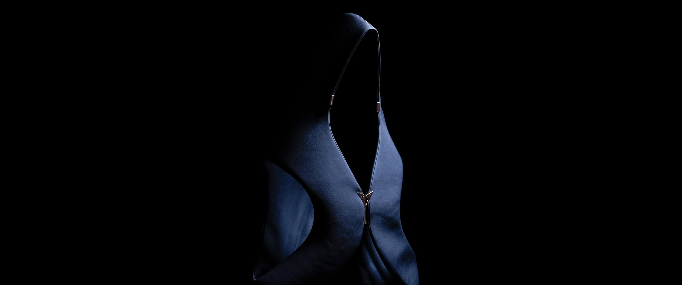 Una prenda oscura con capucha y una cremallera prominente aparece iluminada de forma espectacular sobre un fondo negro, y crea así una imagen de moda abstracta y misteriosa.
