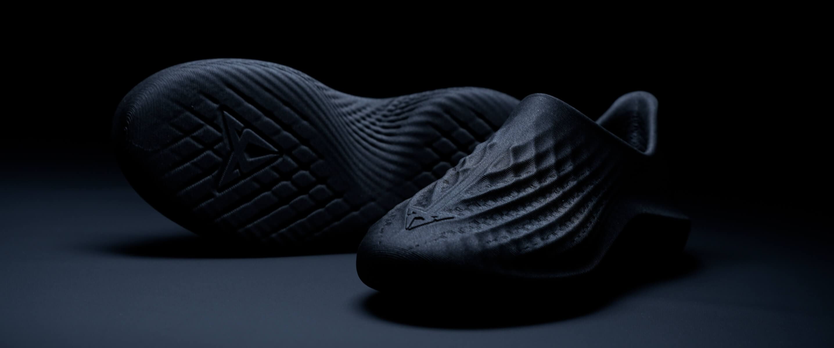 Par de zapatos oscuros, con textura, expuestos en una foto de producto sobre un fondo oscuro.