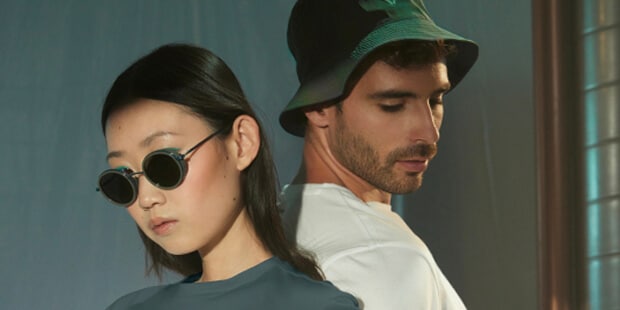 Dos modelos; una chica con pelo oscuro con gafas de sol y camiseta azul, el otro, chico, con gorro verde y camiseta blanca con fondo borroso.