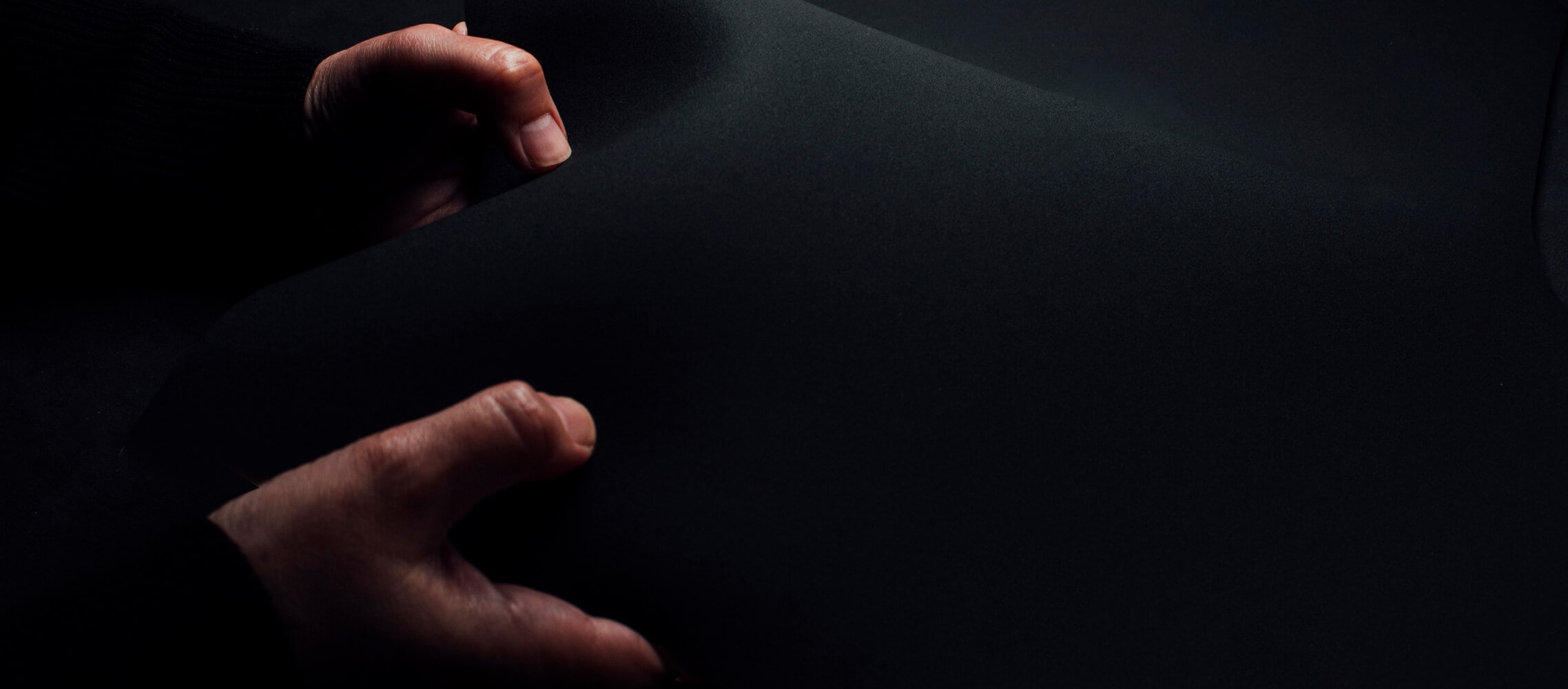 Primer plano de dos manos que sujetan un trozo de material negro con un fondo oscuro que se confunde con el material.