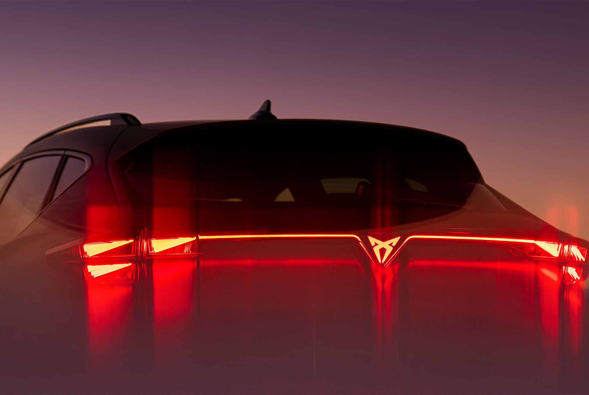 Primer plano de la luz trasera iluminada del nuevo CUPRA Formentor 2024, que muestra un diseño anguloso y un brillo rojo sobre el fondo del atardecer.