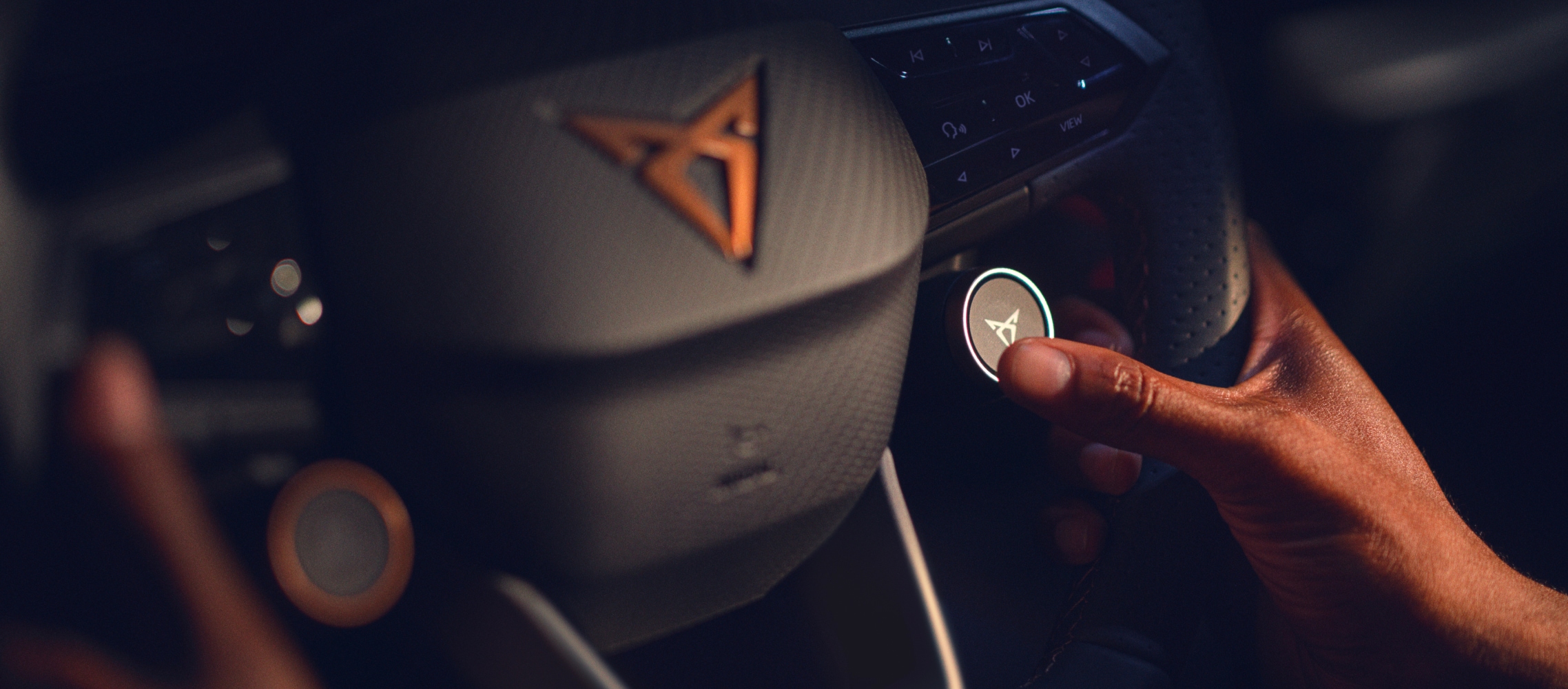 Volante del CUPRA Born con botones satélite y logotipo CUPRA con detalles en cobre, primer plano del interior del coche de empresa.