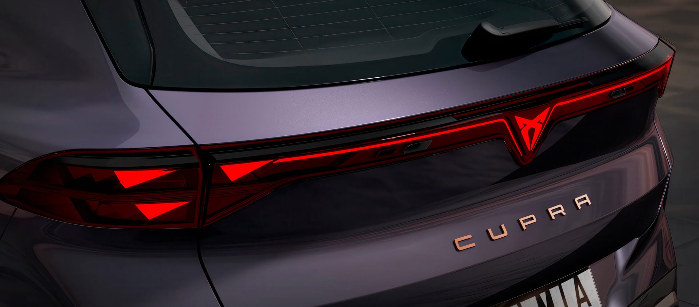Primer plano de la parte trasera del CUPRA Terramar vz en color Dark Void, faros traseros del PHEV con el logotipo de CUPRA iluminado y letras con detalles en cobre.