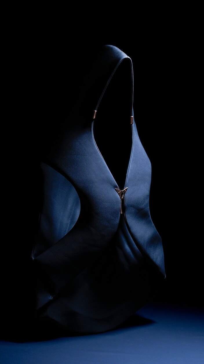 Imagen minimalista de una persona vistiendo un atuendo oscuro con capucha y detalles metálicos en un fondo negro