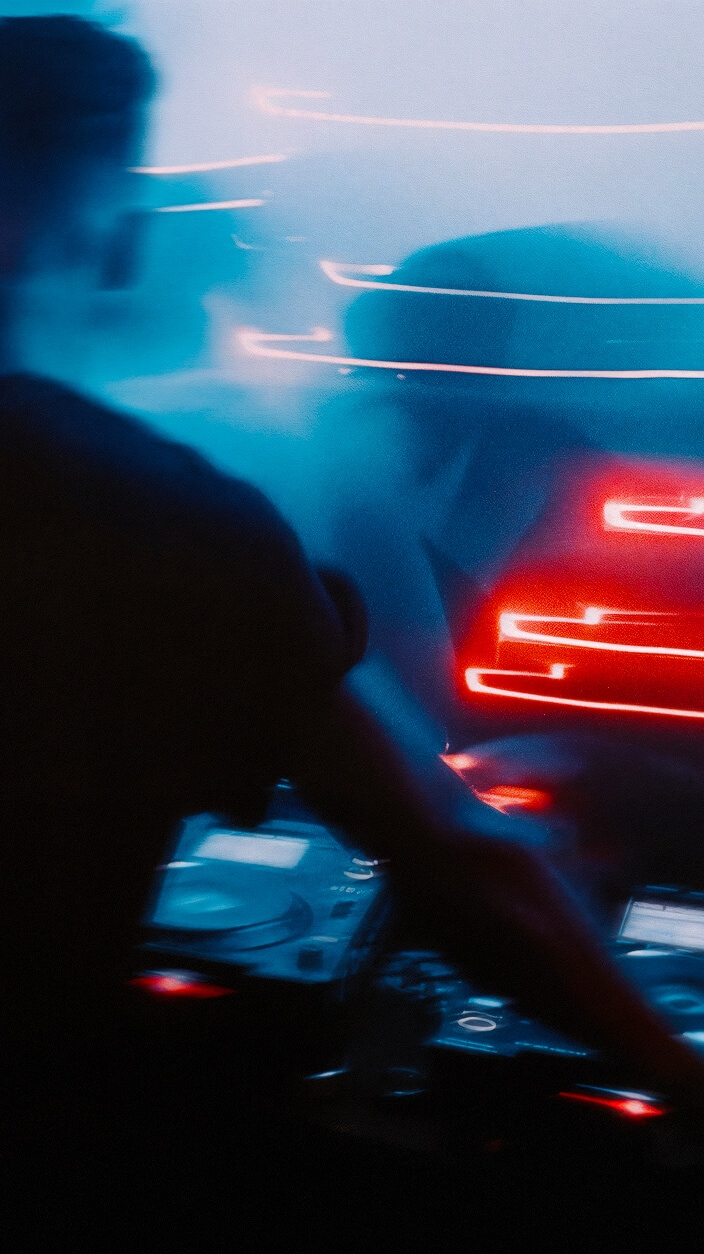 Imagen desenfocada de un DJ con equipamiento, rodeado por franjas de luz brillantes de color rojo y azul con un evento musical frente a él