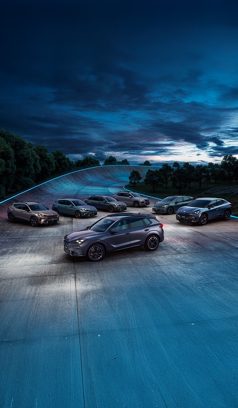 Formación de todos los coches de la gama CUPRA frente a curva peraltada de un circuito al anochecer. Una franja de luz azul sigue la curva del circuito en el fondo