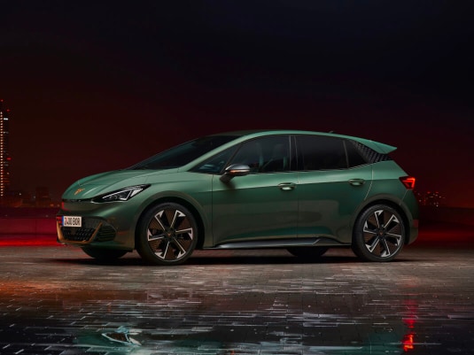 CUPRA Born eléctrico color rojo oscuro en un estudio con iluminación ambiental cálida y tonos metálicos.