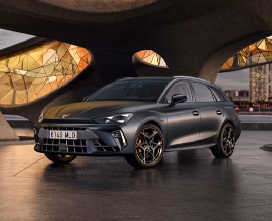 CUPRA León Sportstourer color gris oscuro estacionado al aire libre con paisaje urbano al fondo.