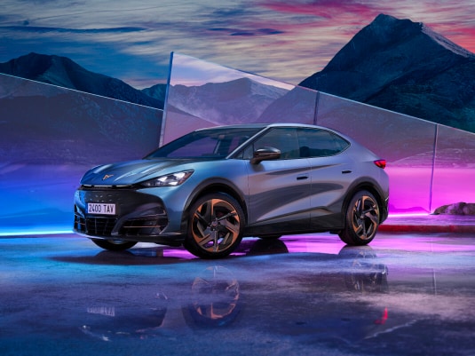 CUPRA Tavascan eléctrico color azul con luces LED encendidas en un entorno futurista con neones y reflejos.